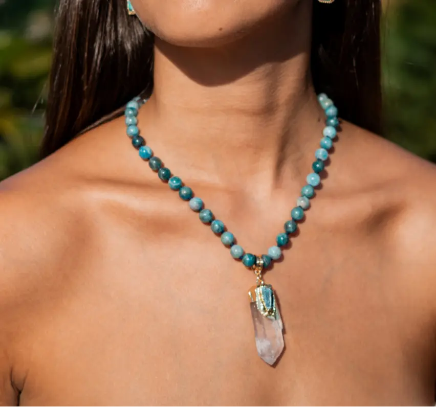 Woman wearing a blue beaded necklace with a clear pendant outdoors